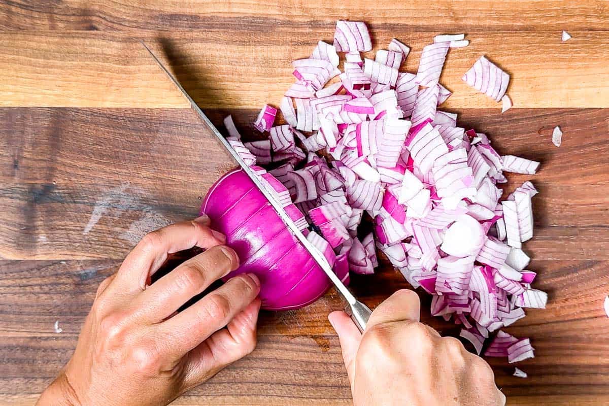 Dicing up red onion on a wood cutting board with a chefs knife.