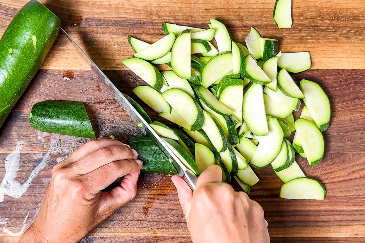 Cutting the zucchini into half moon slices on a wood cutting board with a chefs knife.