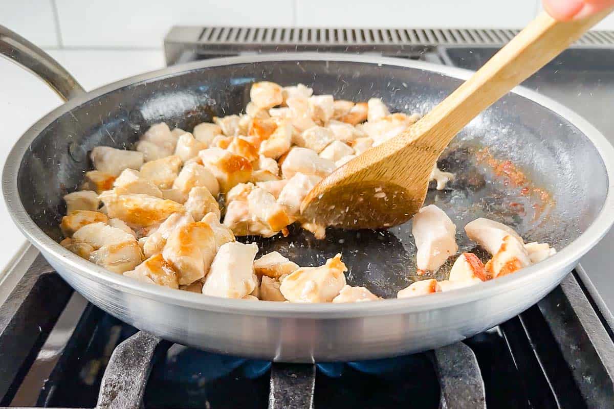Sautéing the chicken in a large skillet with a wood spoon.