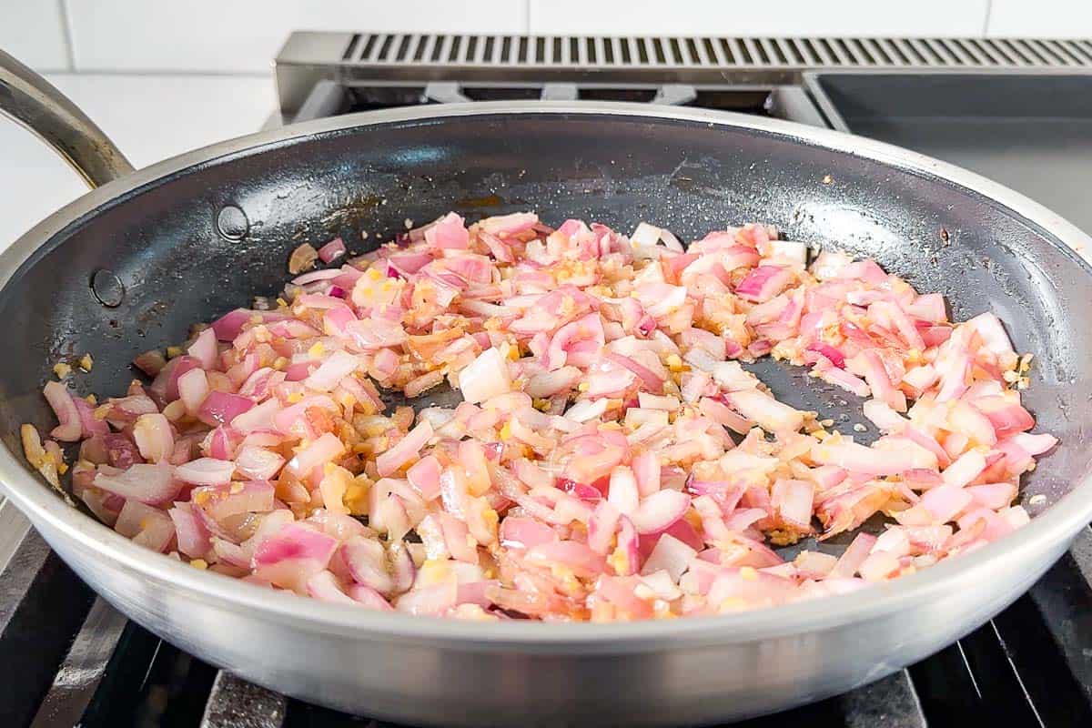 Sautéing the red onion, garlic, and ginger in a large skillet.