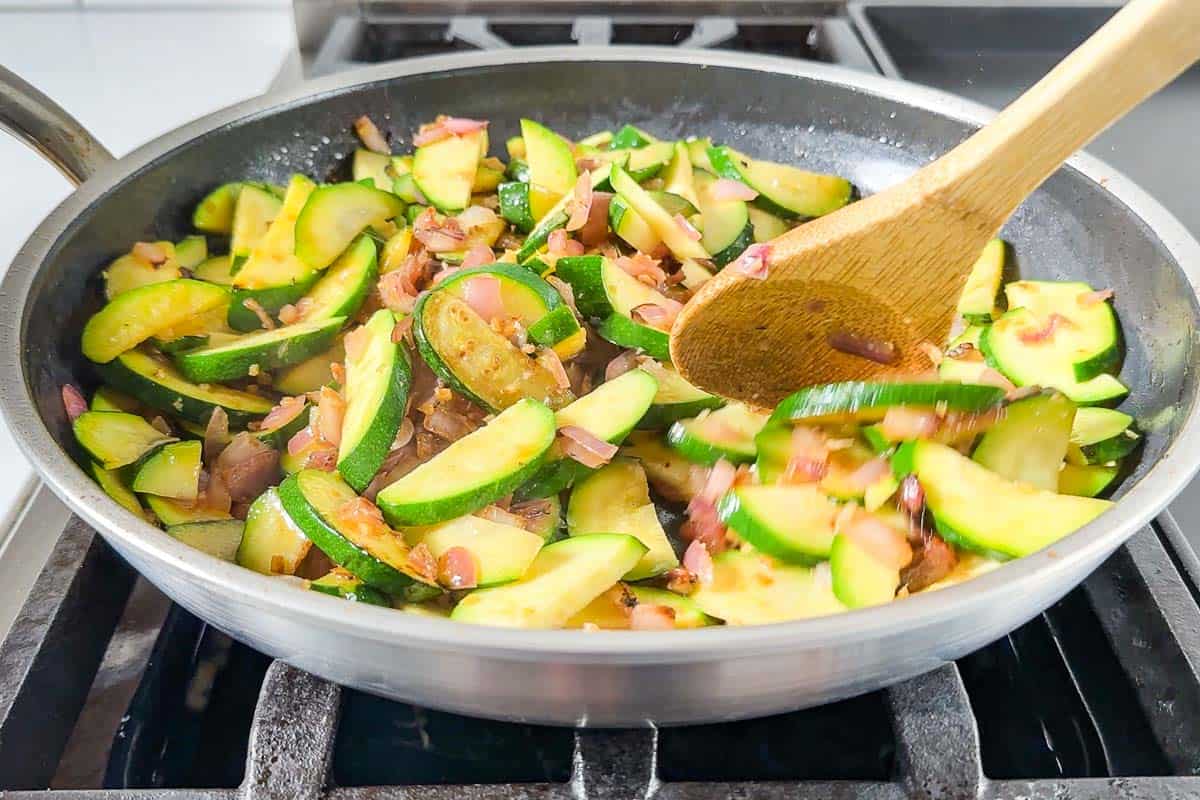 Adding the zucchini to the pan and stir frying until browned.