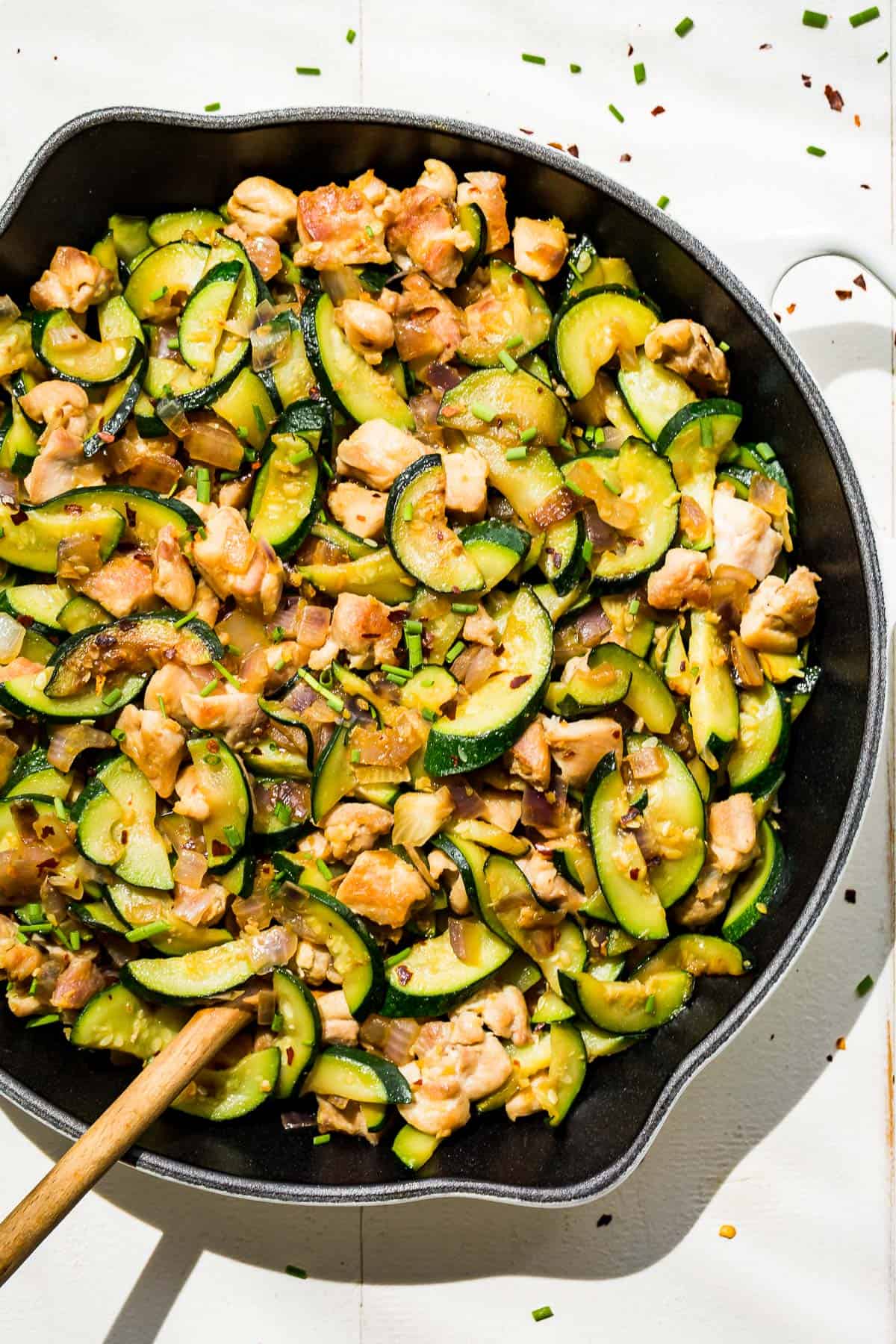 Straight down view of Chicken Zucchini Stir Fry in a white cast iron skillet with a wood spoon in it.