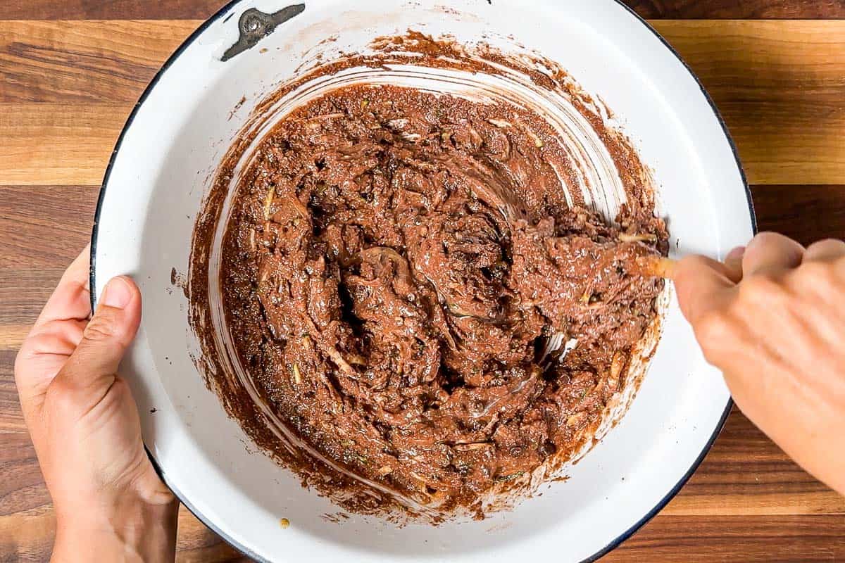 Mixing the wet ingredients into the large white bowl to form the batter for the healthy chocolate zucchini muffins.