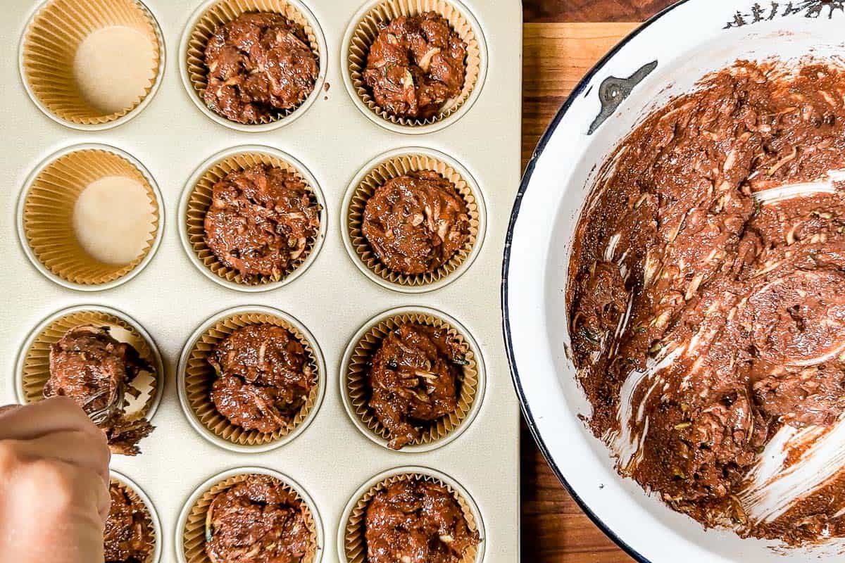 Portioning out the batter for chocolate zucchini muffins into a muffin tin with liners.