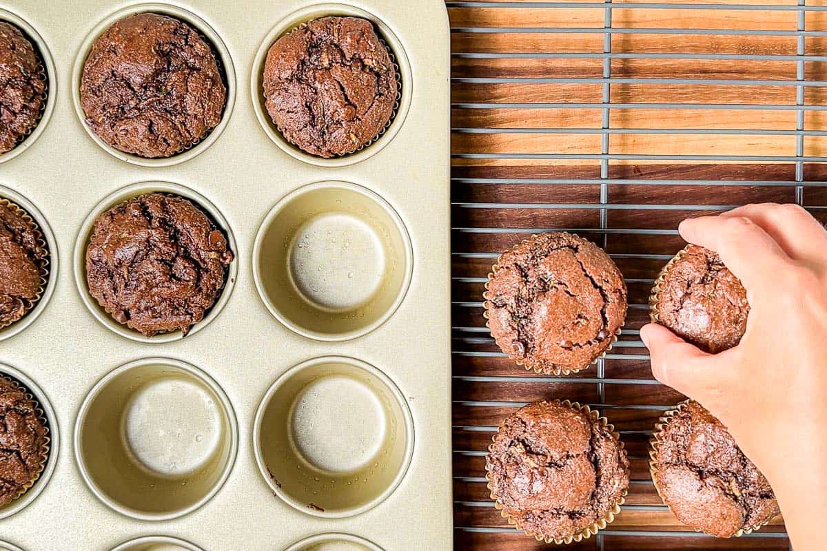 Removing the healthy chocolate zucchini muffins from the muffin tin onto a wire cooling rack.