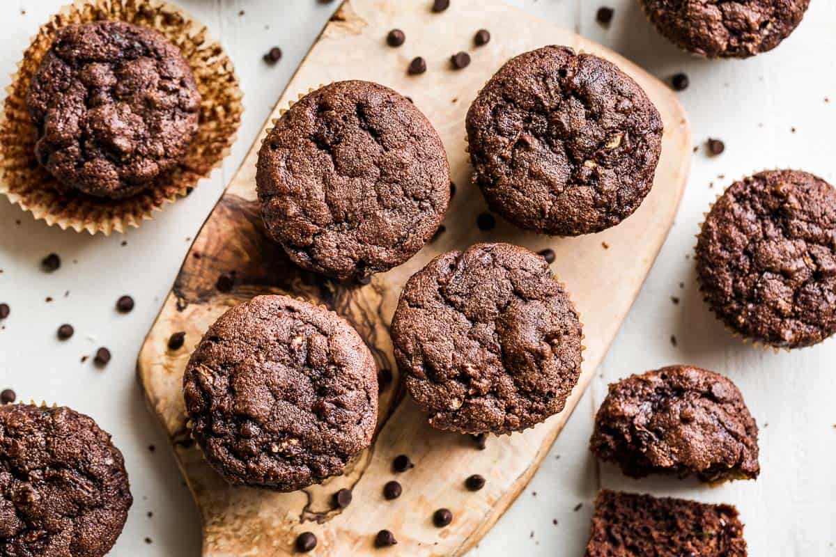 Healthy Chocolate Zucchini Muffins on a wood cutting board with chocolate chips scattered around them.