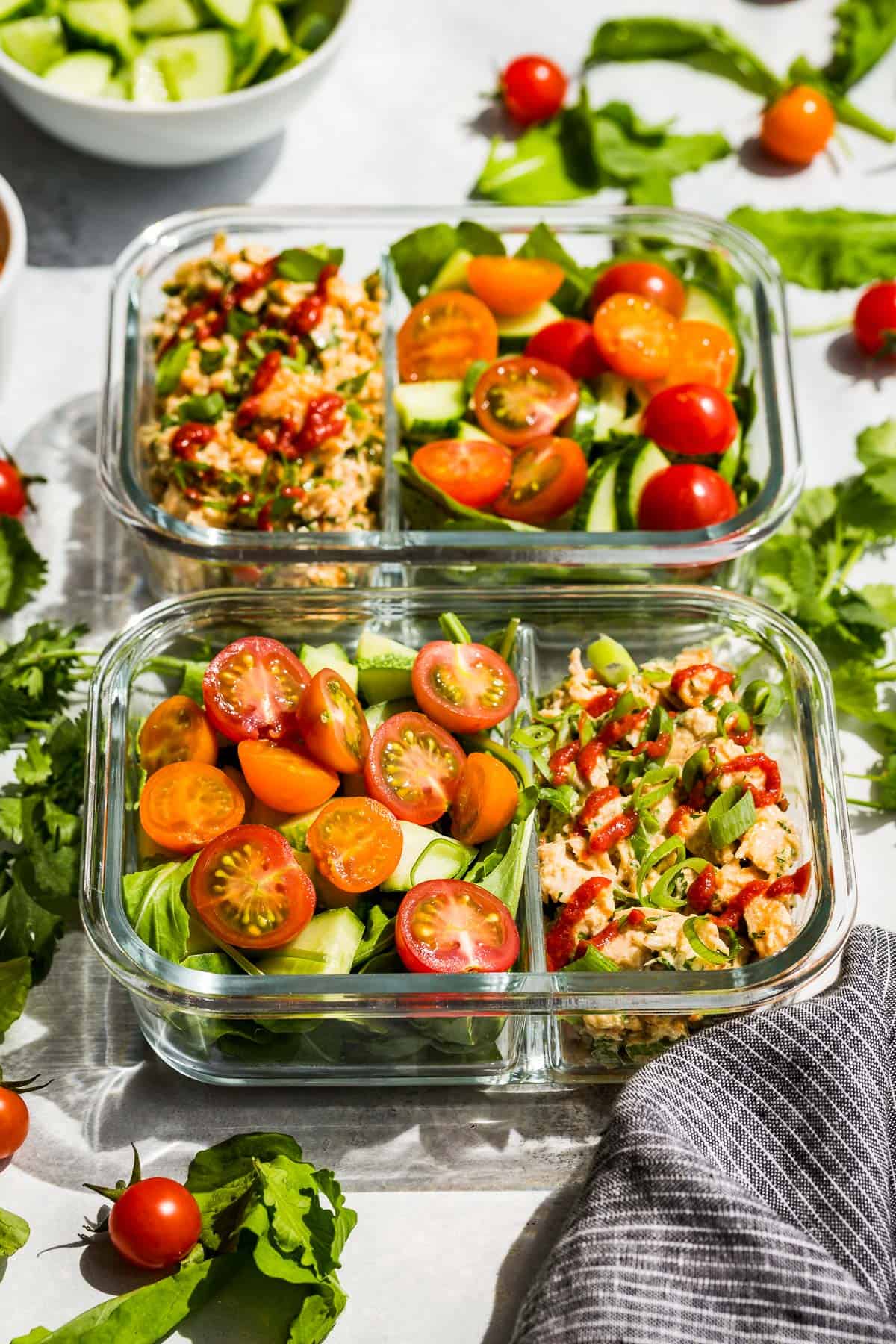 Side view of Spicy Tuna Salad in two meal prep containers with cherry tomatoes and cucumbers on one side.