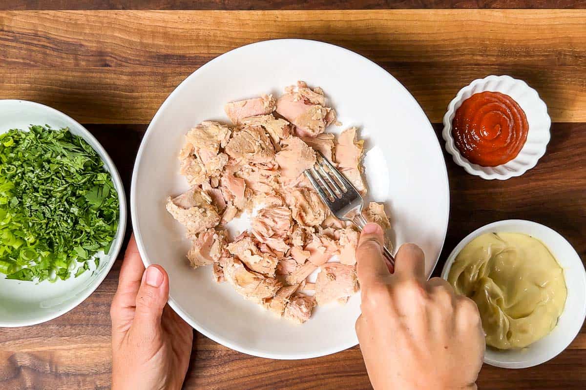 Mashing up the canned tuna fish in a large white bowl.