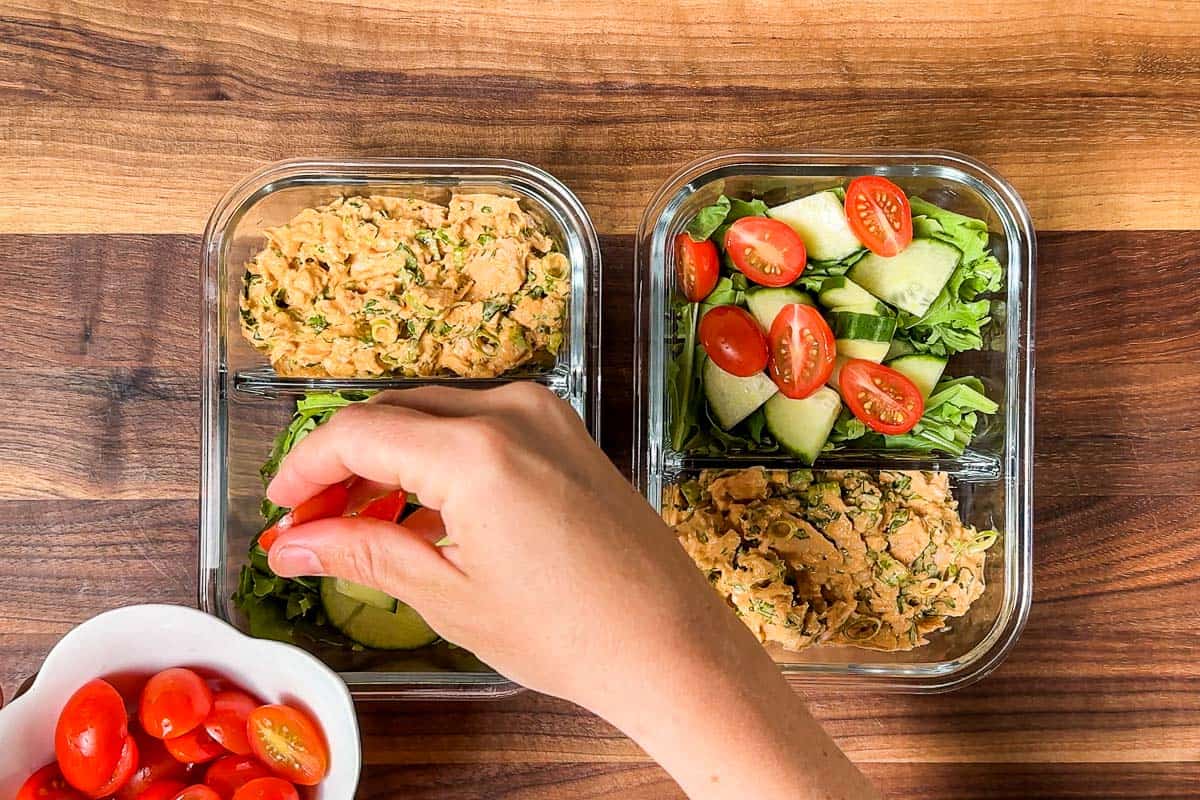 Portioning out the spicy tuna salad into meal prep containers with salad on the other side.