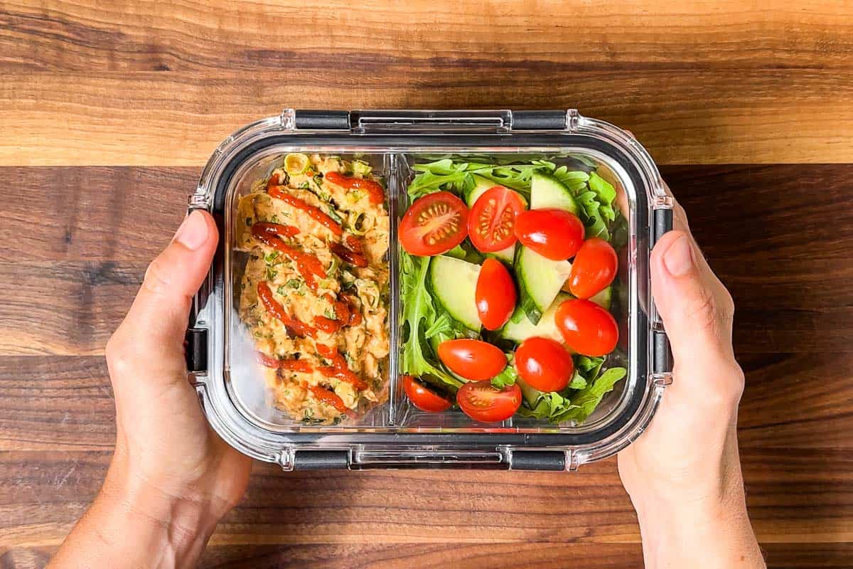 Adding sriracha and a lid to the finished spicy tuna salad meal prep containers.