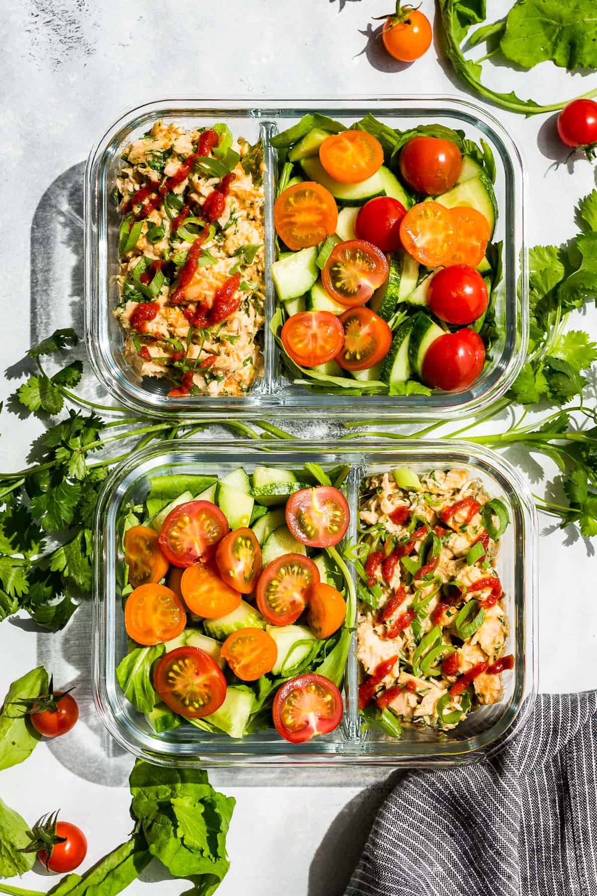 Straight down view of Spicy Tuna Salad in meal prep containers with cherry tomatoes and chopped cucumbers on the side.
