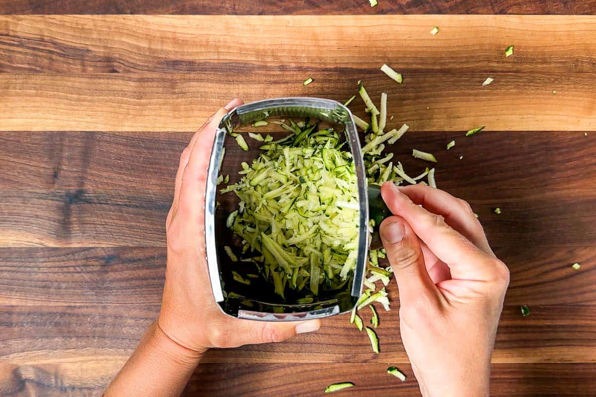 Grating zucchini on a wood cutting board.