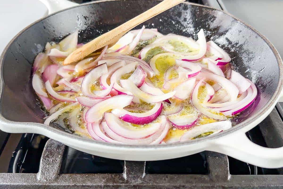 Sautéing the red onion in butter in a large white cast iron skillet.