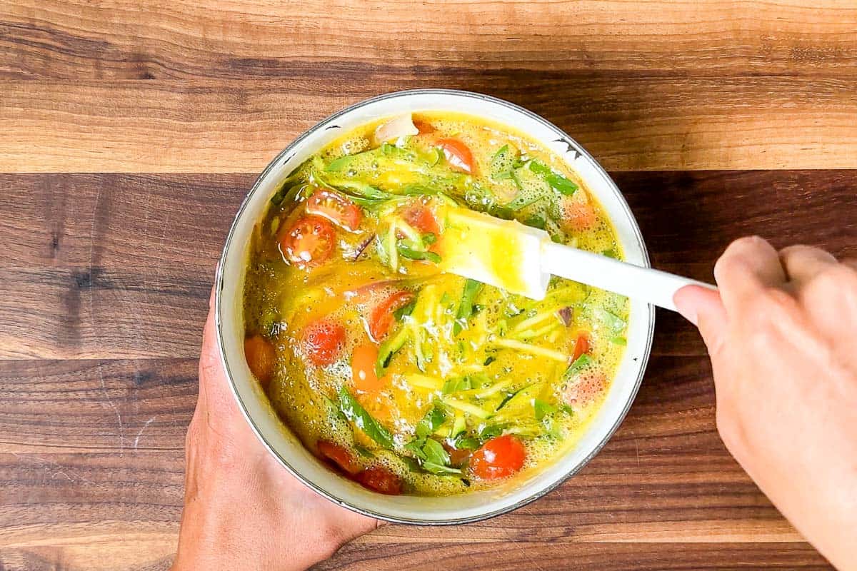 Mixing the veggies into the egg mixture in a white bowl.