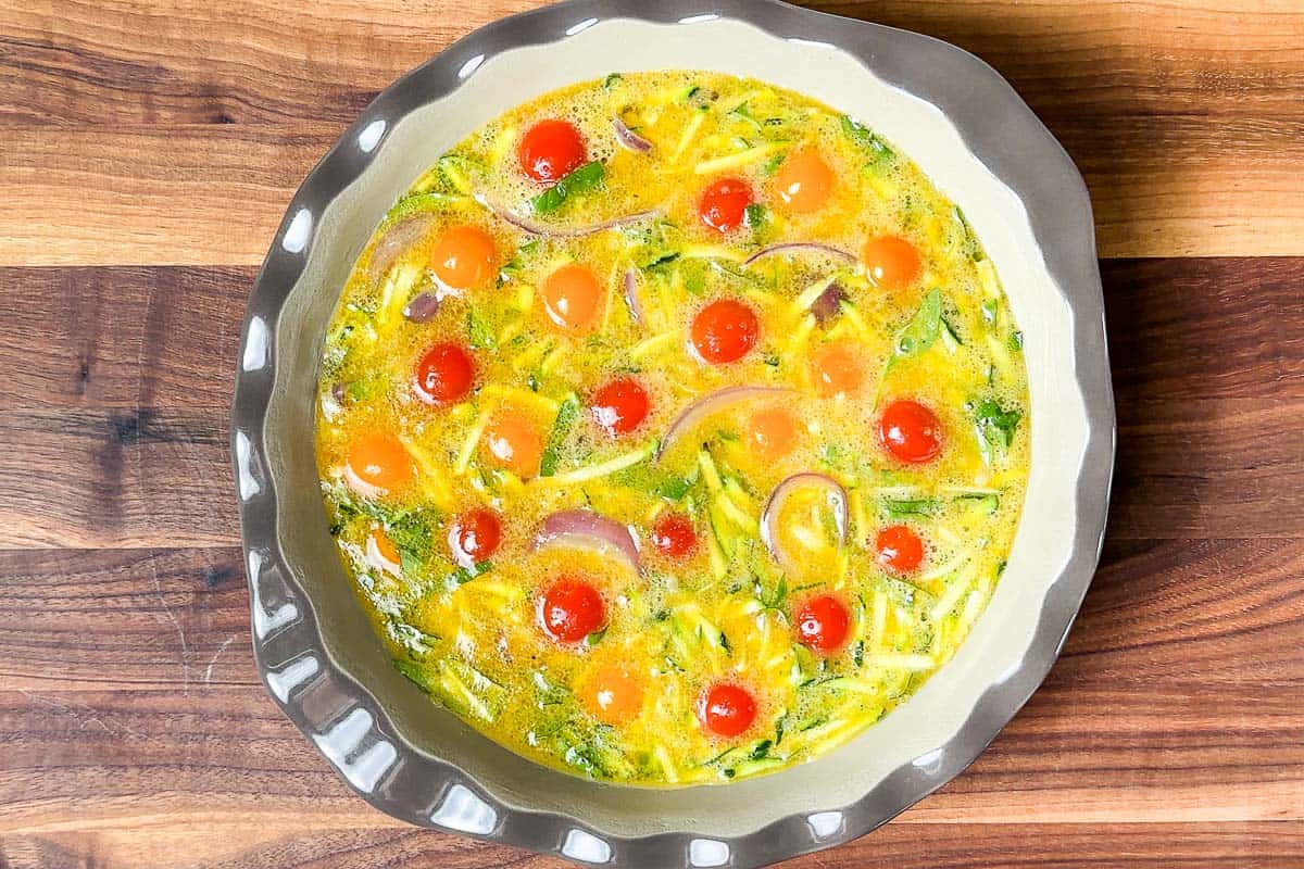 Adding the egg veggie mixture into a greased pie plate.