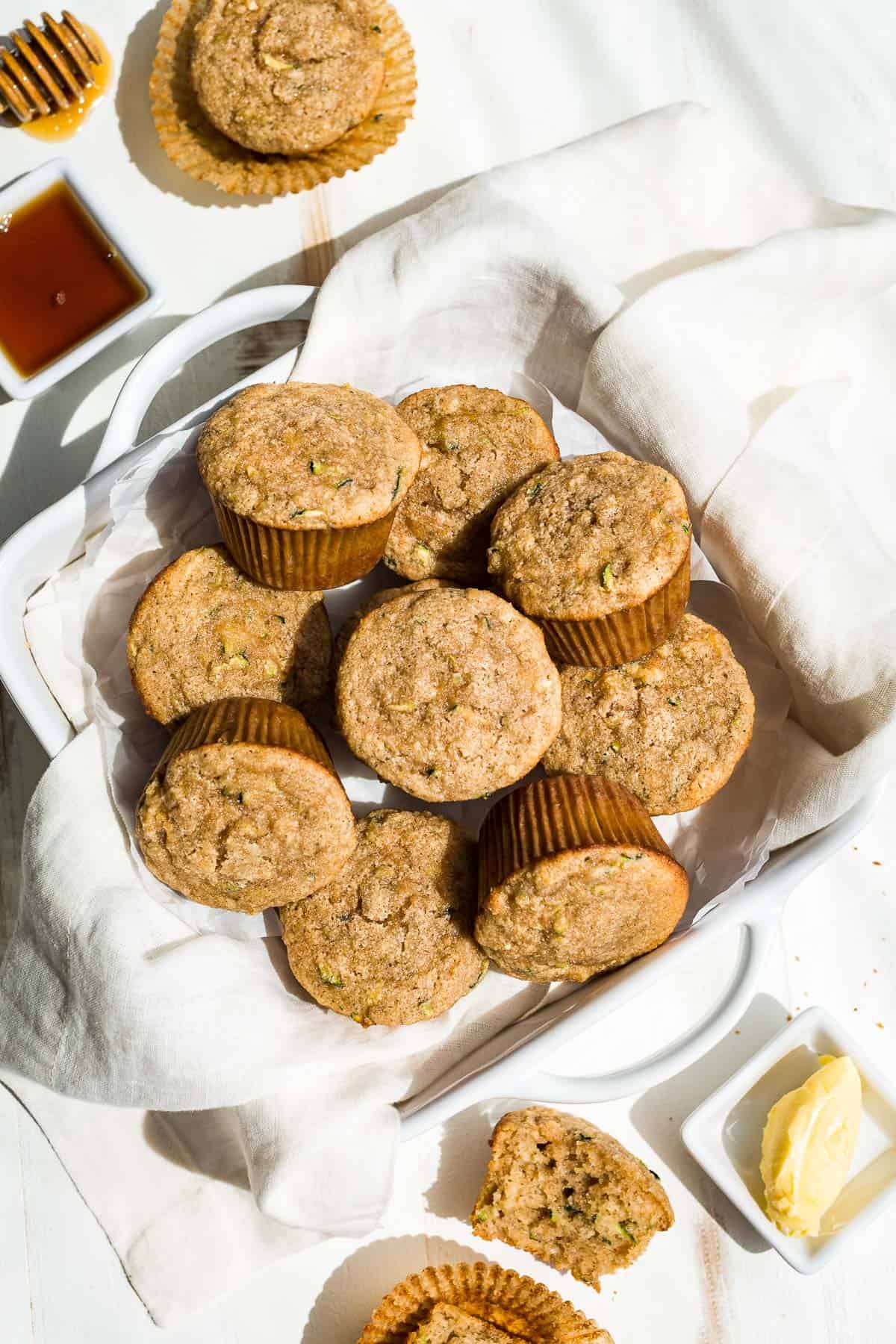 Straight down view of almond flour pineapple zucchini muffins in a cloth lined square dish with butter and honey on the side.