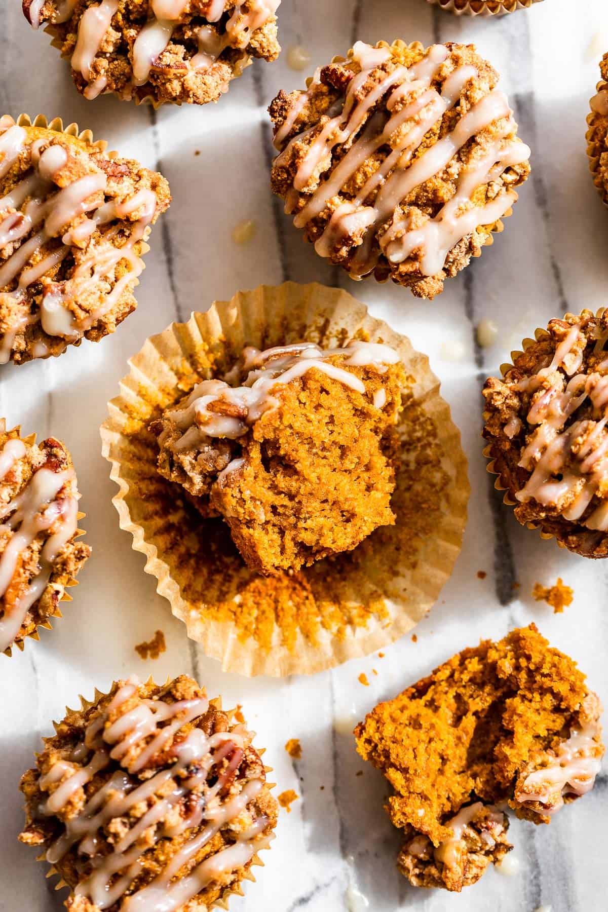 Straight down view of almond flour pumpkin muffins on a white background with one split open.