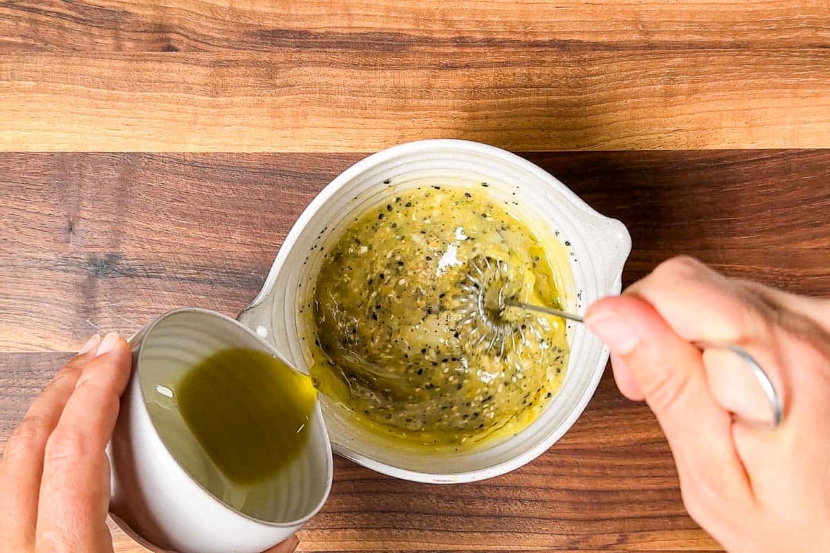 Whisking the olive oil into the everything bagel dressing in a small pottery bowl.