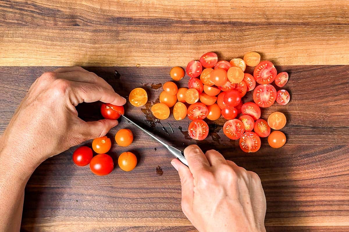 Cutting up the cherry tomatoes with a pairing knife on a wood cutting board.