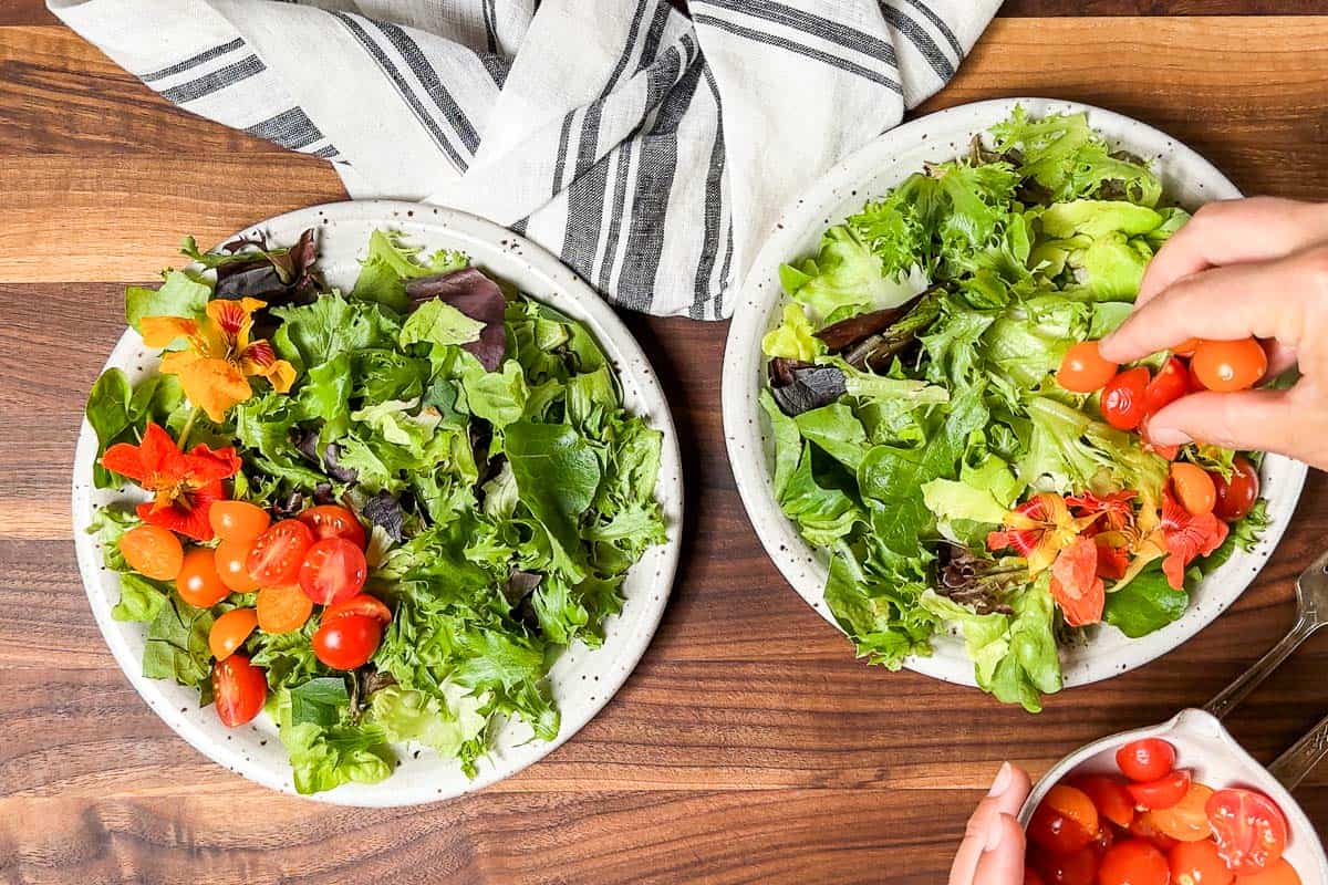 Adding the greens and cherry tomatoes to two salad bowls.