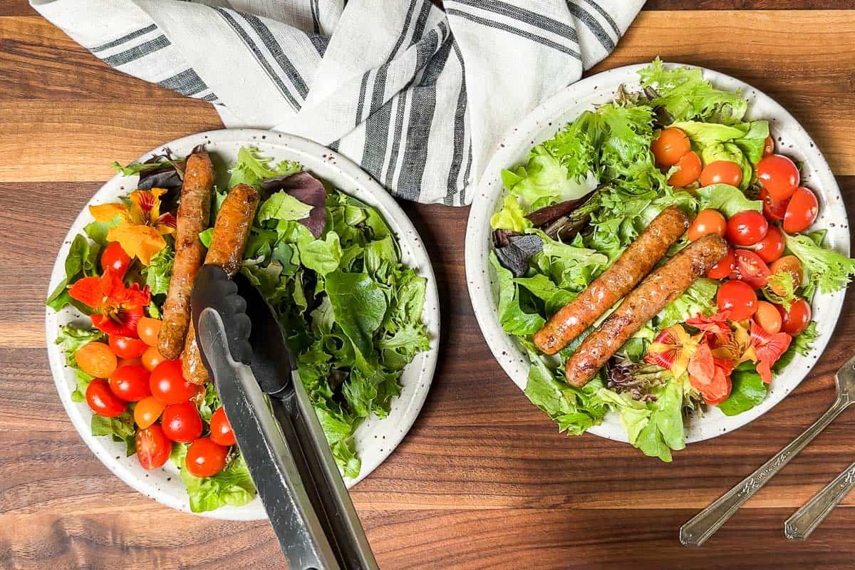 Adding the sausage links with a pair of tongs to the breakfast salad plates.