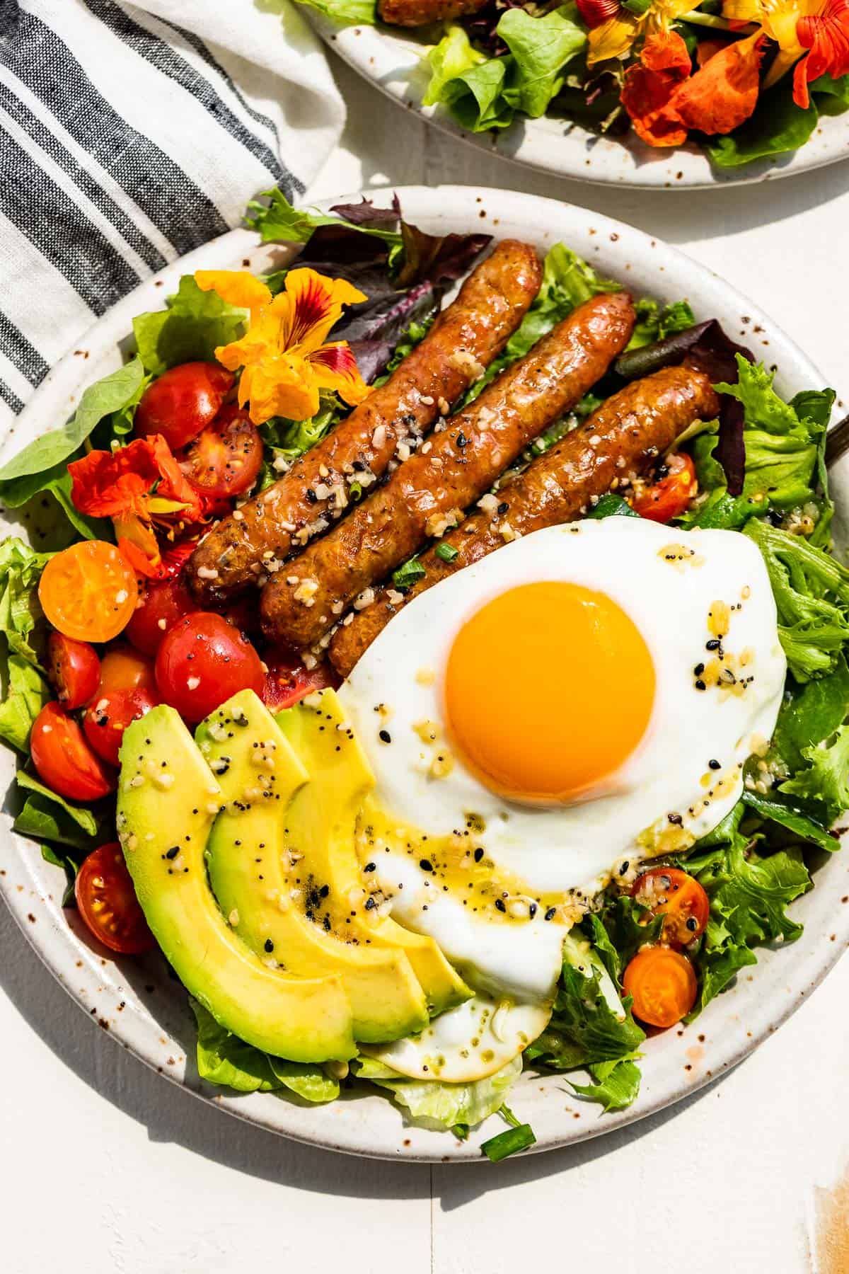 Straight down view of Breakfast Salad on a pottery plate topped with an over easy egg and sliced avocado.