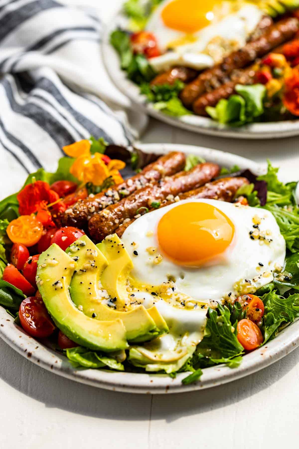 Side view of Breakfast Salads on two plates topped with over easy eggs and sliced avocado.