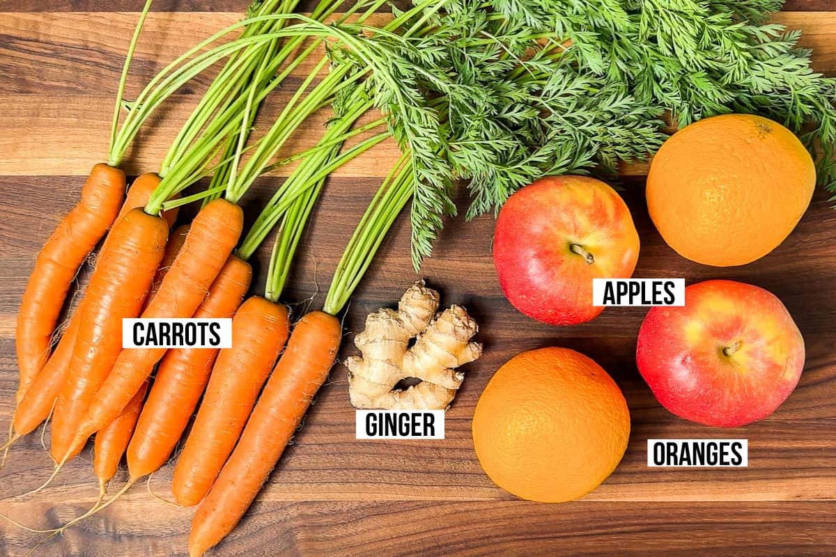 Carrot, ginger root, oranges, and apples on a wood cutting board.