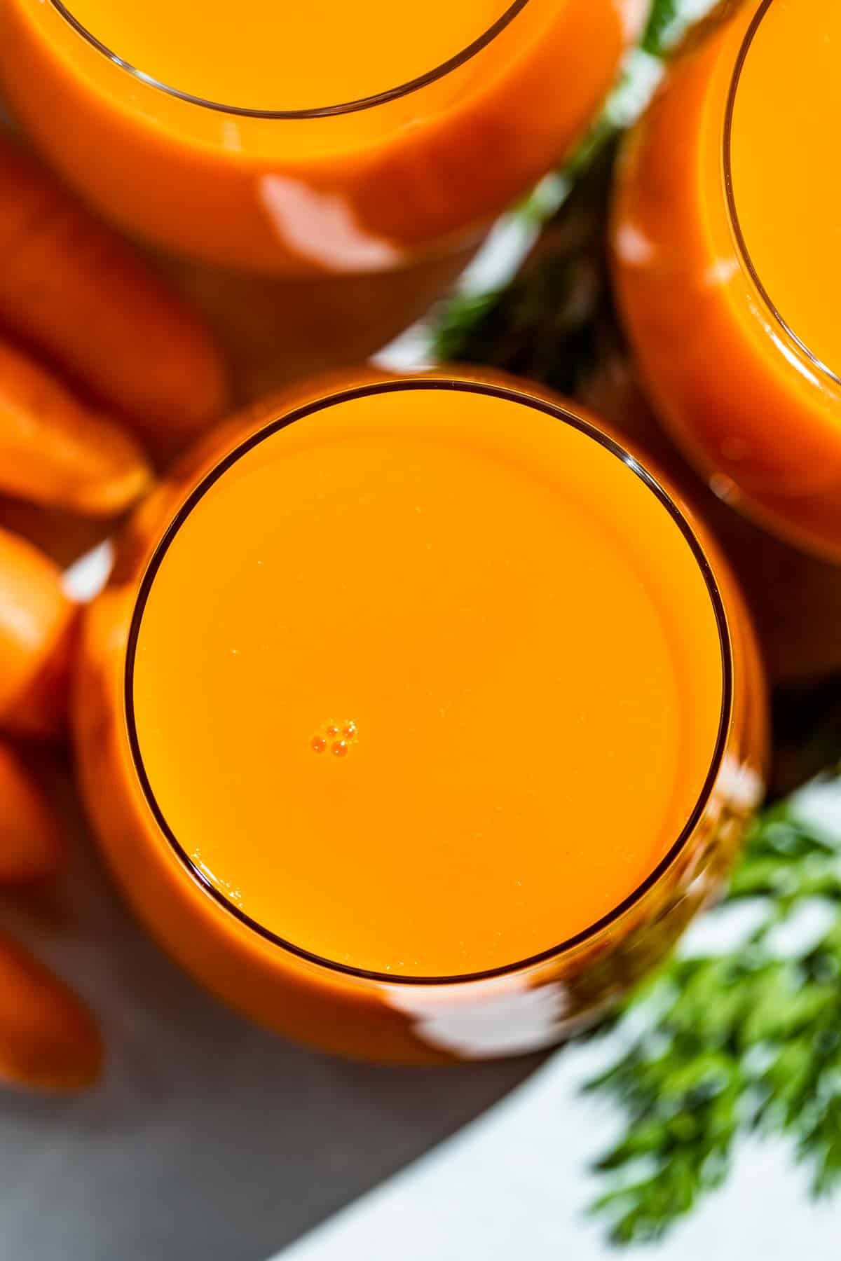 Close up straight down view of carrot juice in three glasses.