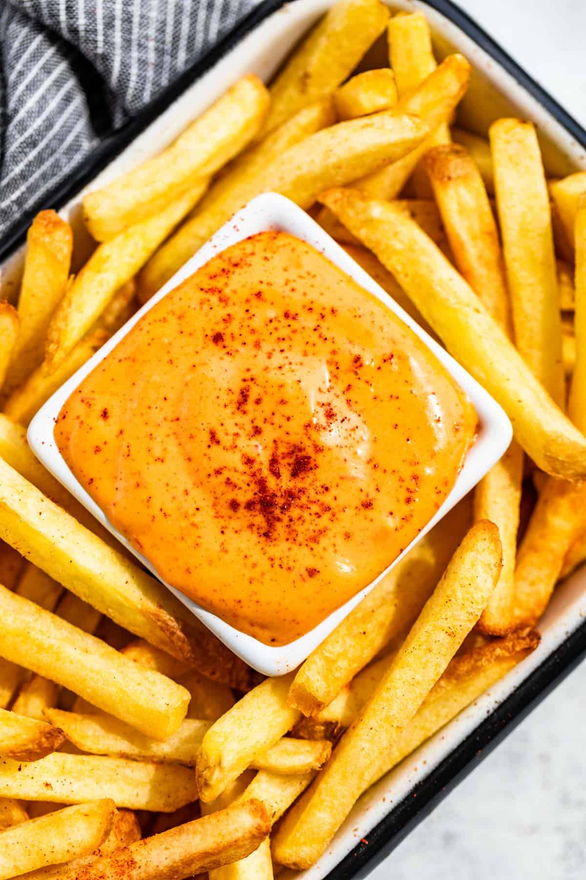 Straight down view of French fries in a square container on the diagonal with a square dish of Chipotle Aioli in the center.