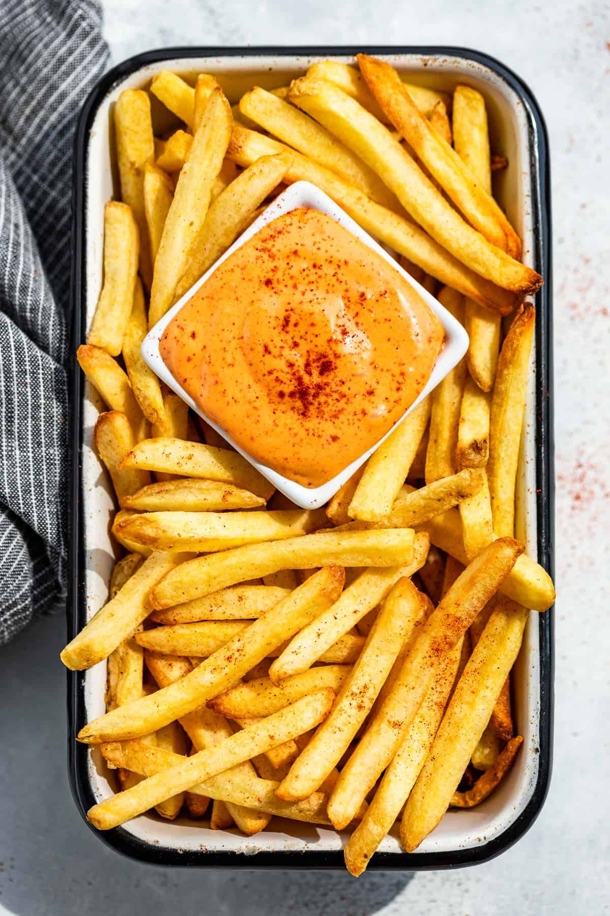 Straight down view of French fries in a rectangular container with a square dish of Chipotle Aioli in the center.