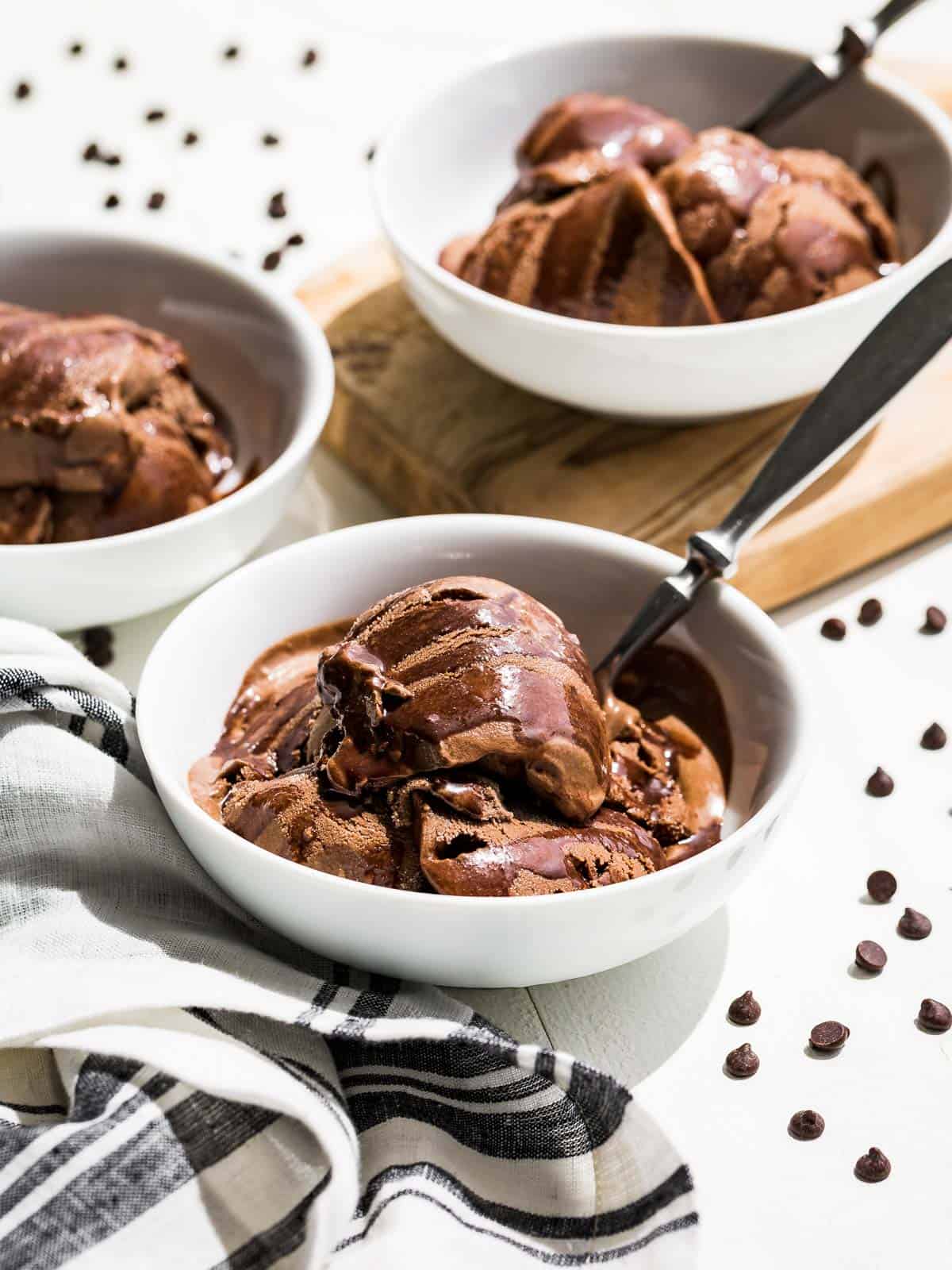 Three bowls of Chocolate Avocado Ice Cream drizzled with chocolate sauce and chocolate chips sprinkled on the side.