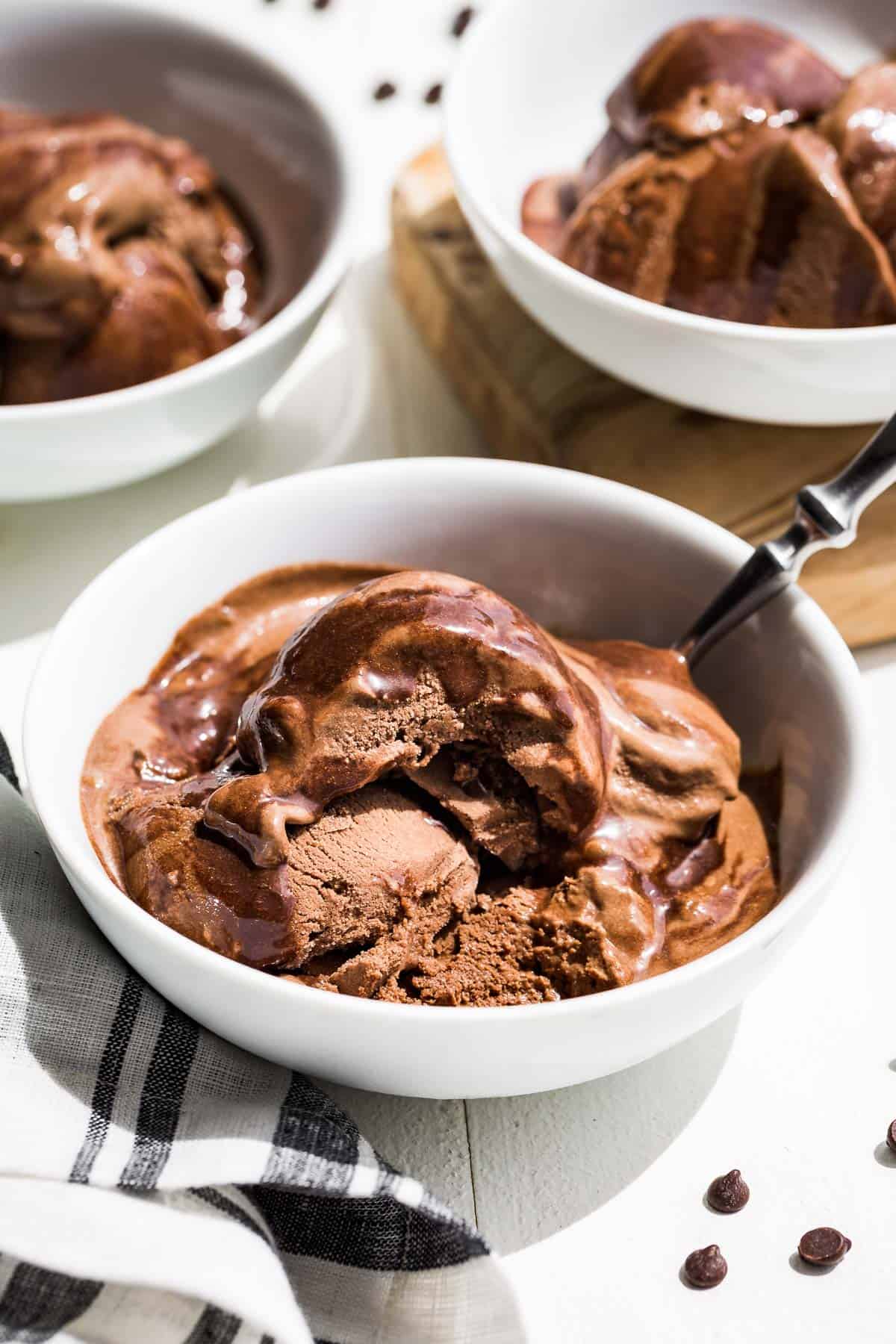 Three white bowls of chocolate avocado ice cream drizzled with chocolate sauce and bite taken out of the front bowl.