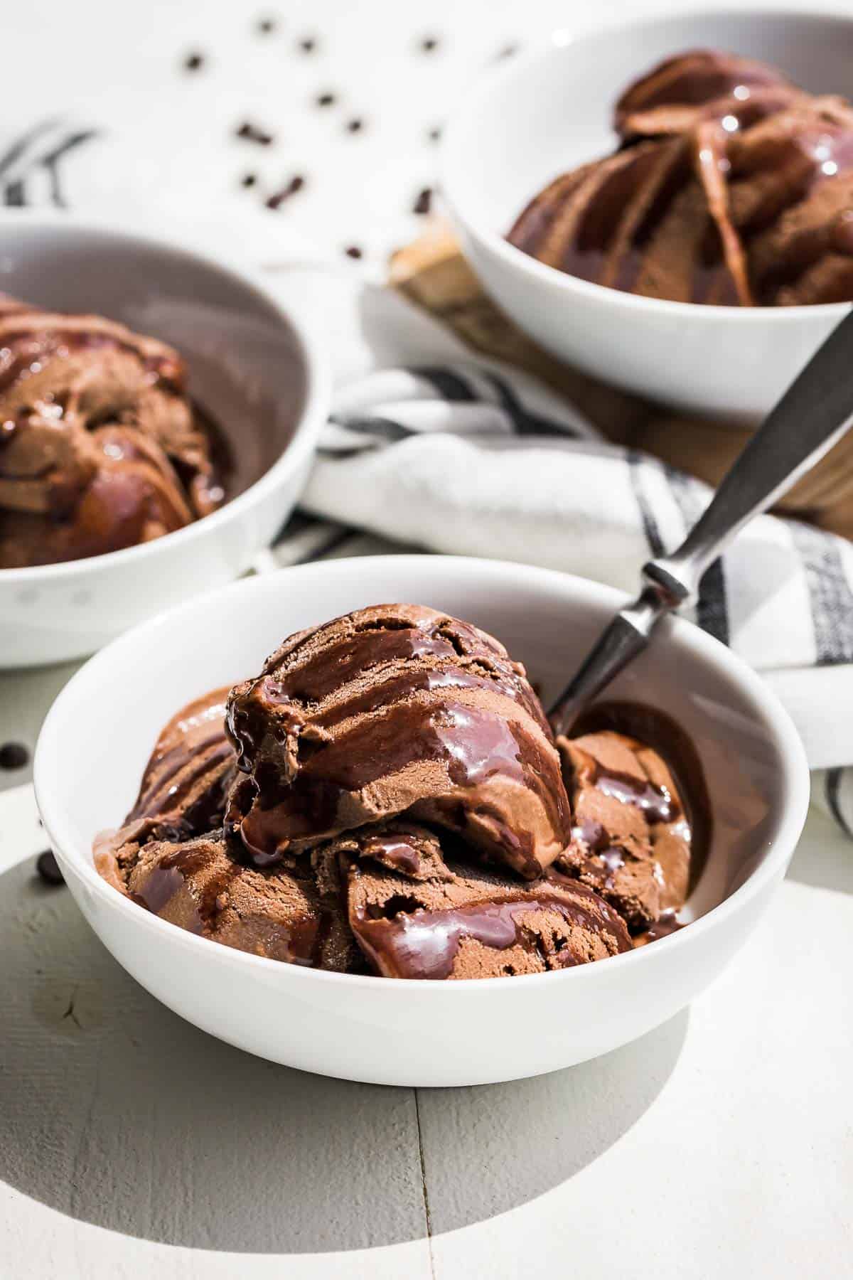 Side view of three white bowls filled with chocolate avocado ice cream drizzled with chocolate sauce.