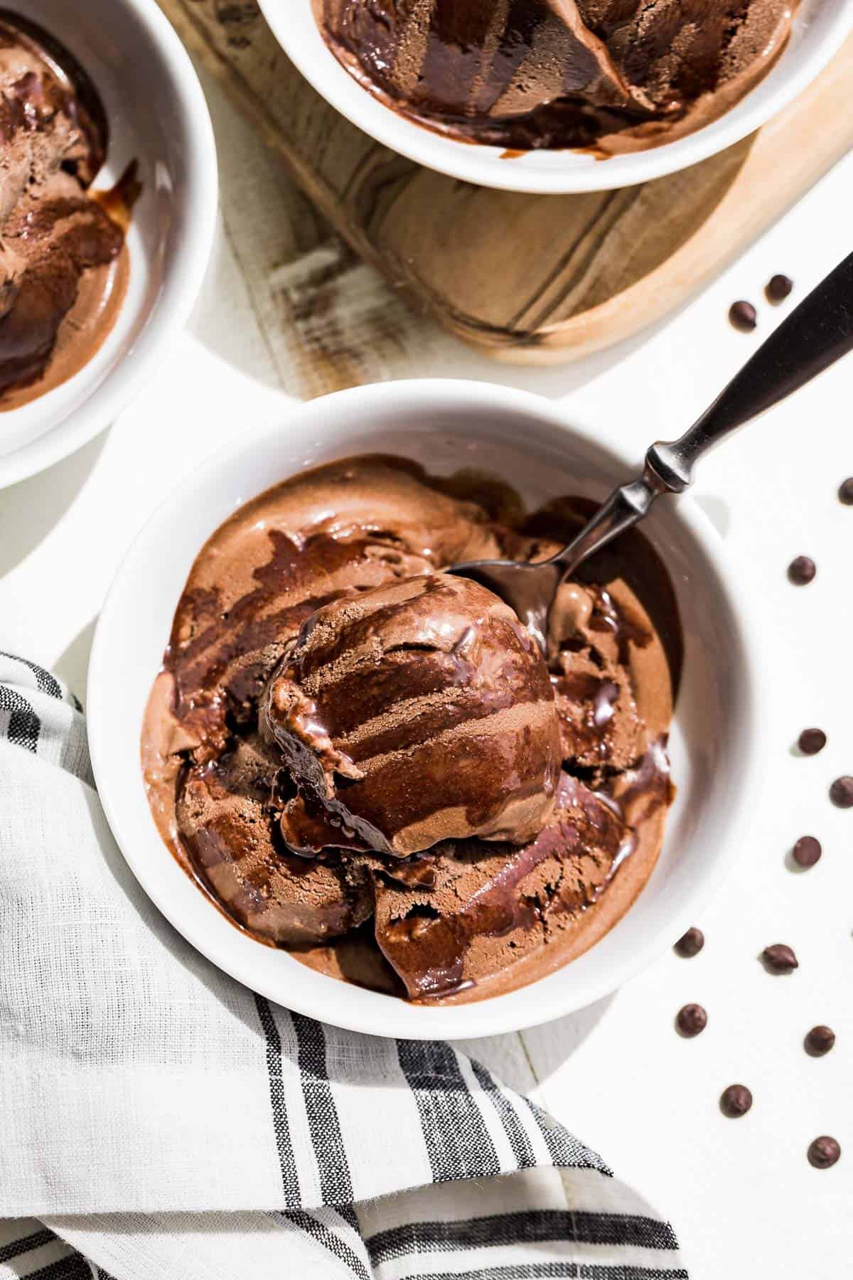 Straight down view of Chocolate Avocado Ice Cream in three white bowls drizzled with chocolate sauce.