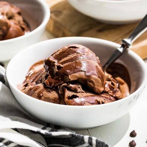 Side view of chocolate avocado ice cream in white bowls drizzled with chocolate sauce and chocolate chips sprinkled on the side.