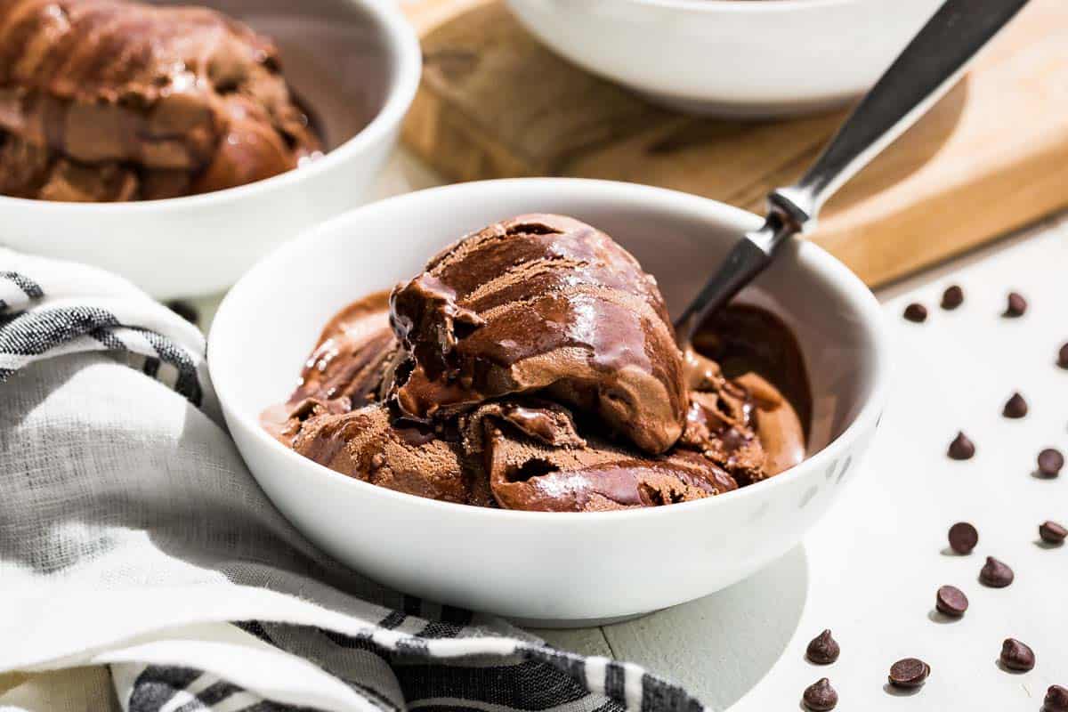 Side view of chocolate avocado ice cream in white bowls drizzled with chocolate sauce and chocolate chips sprinkled on the side.