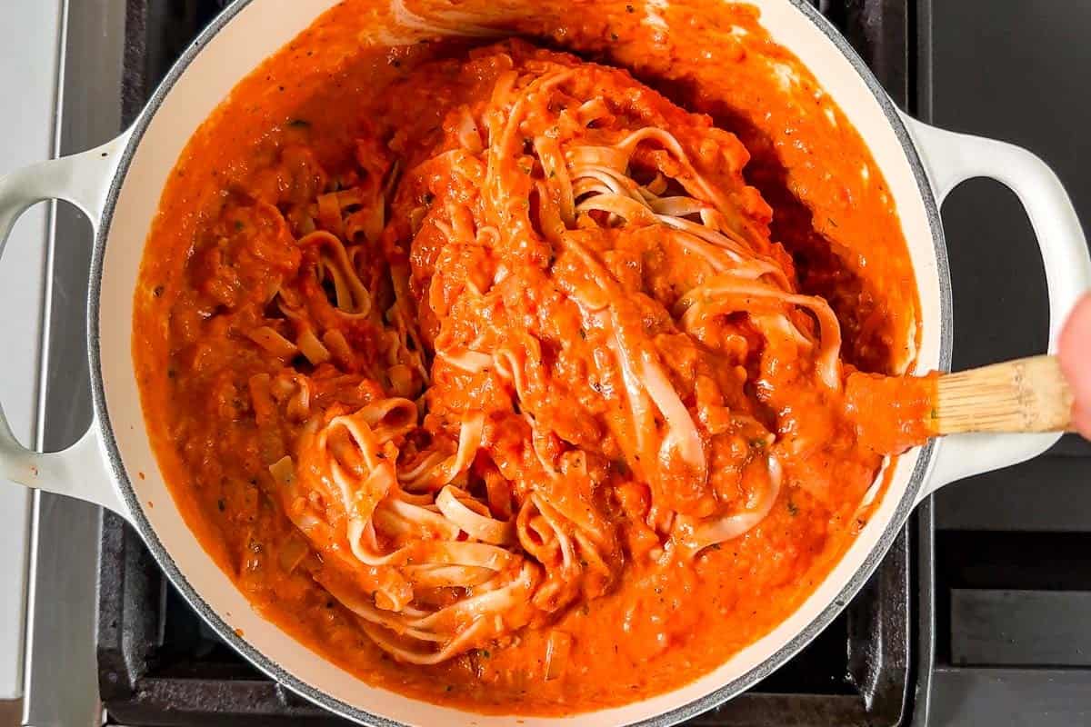 Tossing the cooked pasta together with the creamy tomato sauce in a large pot.