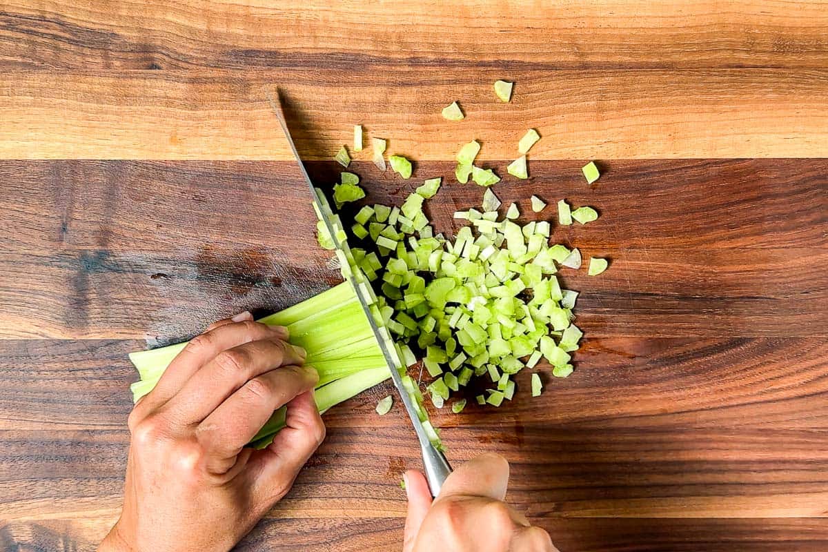 Finely dicing the celery with a chef's knife on a wood cutting board.