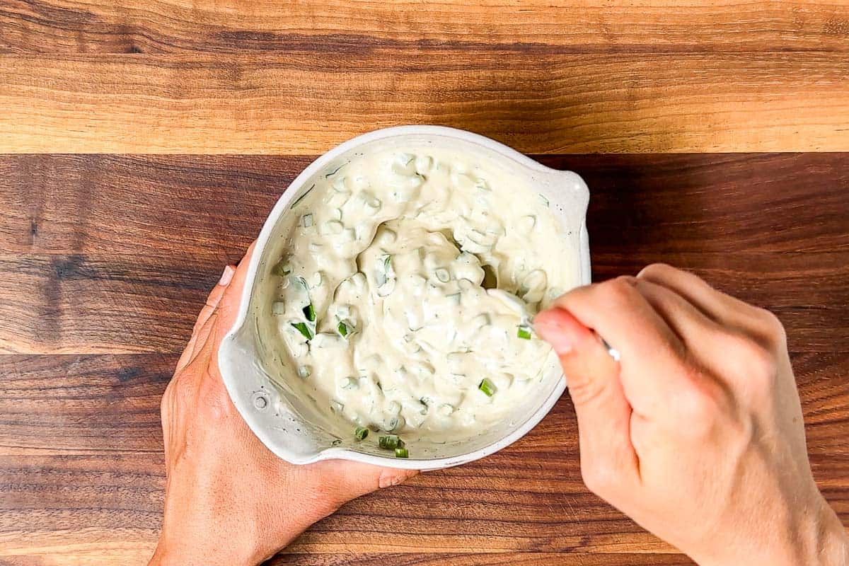 Stirring together the Greek yogurt dressing in a small pottery bowl on a wood cutting board.