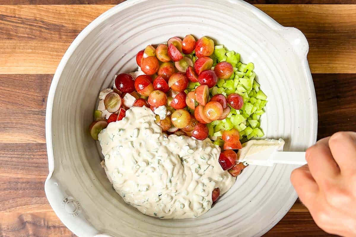 Adding the cooked chicken, grapes, celery, and dressing to a large pottery bowl.