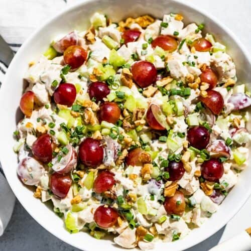 Straight down view of Healthy Chicken Salad topped with grapes with a blue and white linen and wood serving spoons on the side.