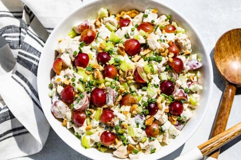 Straight down view of Healthy Chicken Salad topped with grapes with a blue and white linen and wood serving spoons on the side.