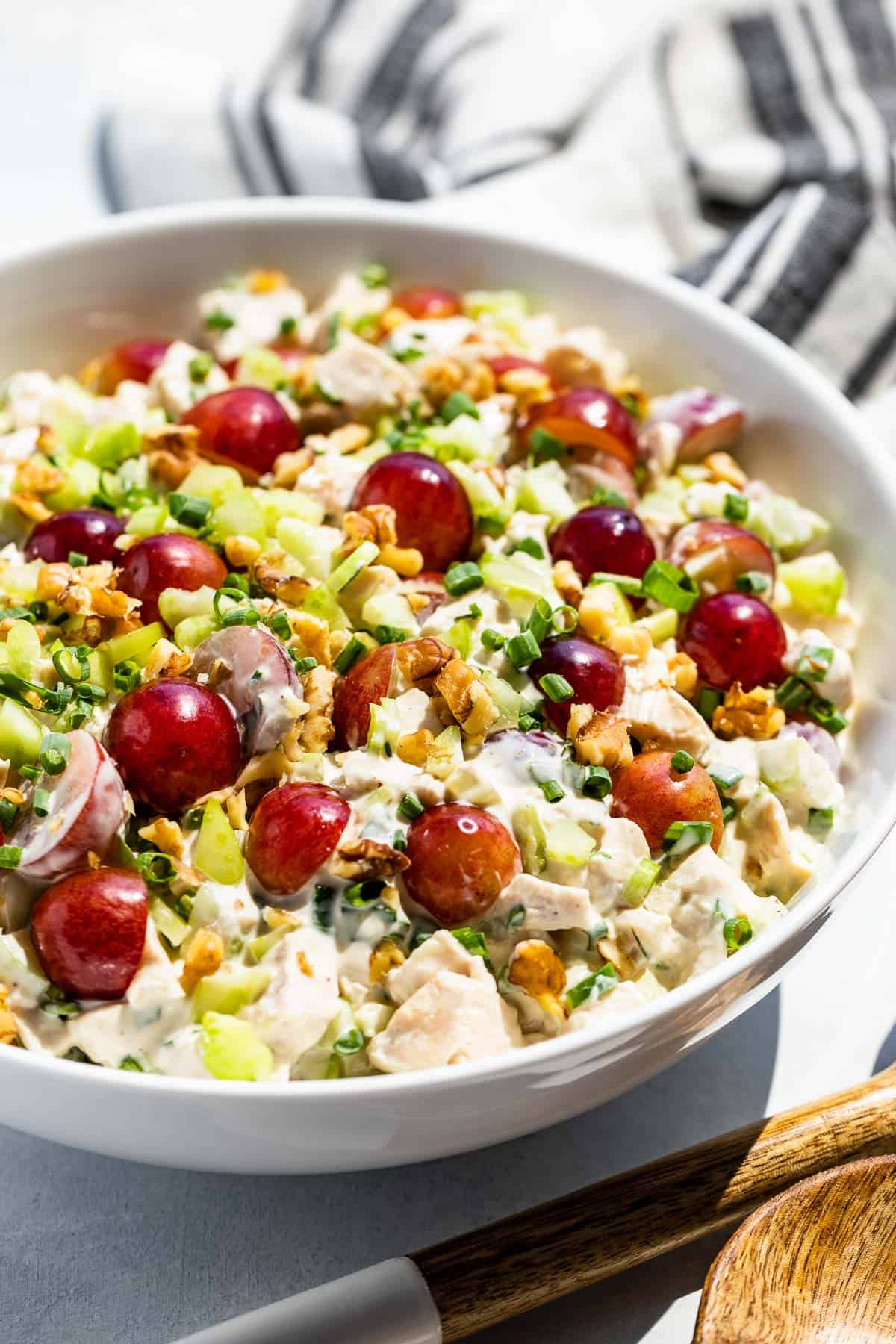 Side view of Healthy Chicken Salad in a white bowl topped with grapes and wood serving spoons on the side.