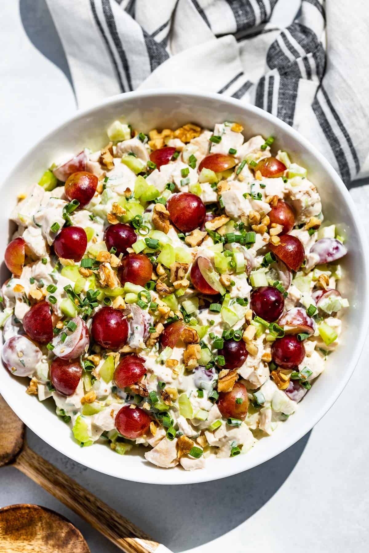 Straight down view of Healthy Chicken Salad in a white bowl topped with grapes and wood spoons on the side.