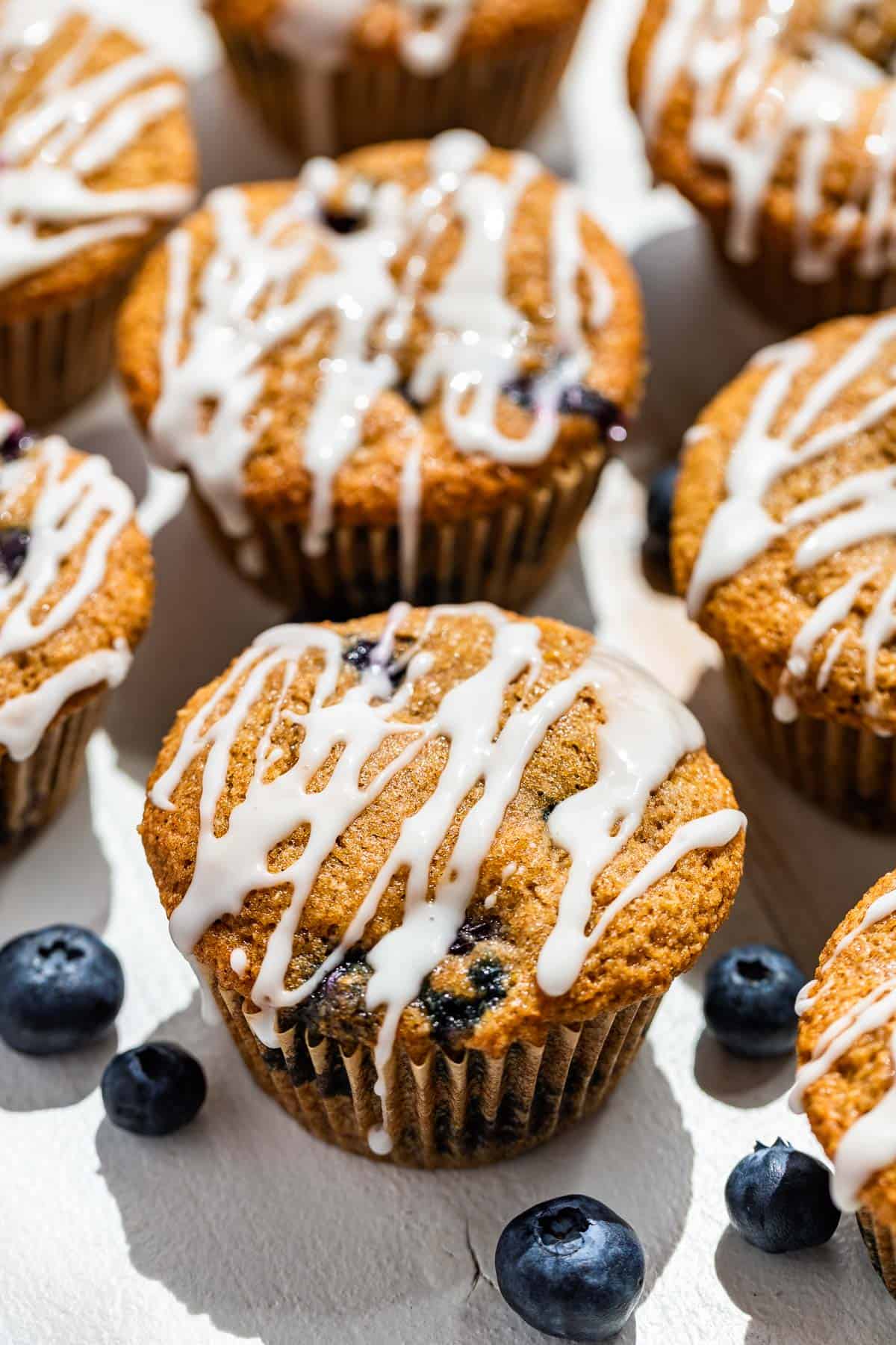 Glazed almond flour blueberry muffins on a white background with a few fresh blueberries on the side.