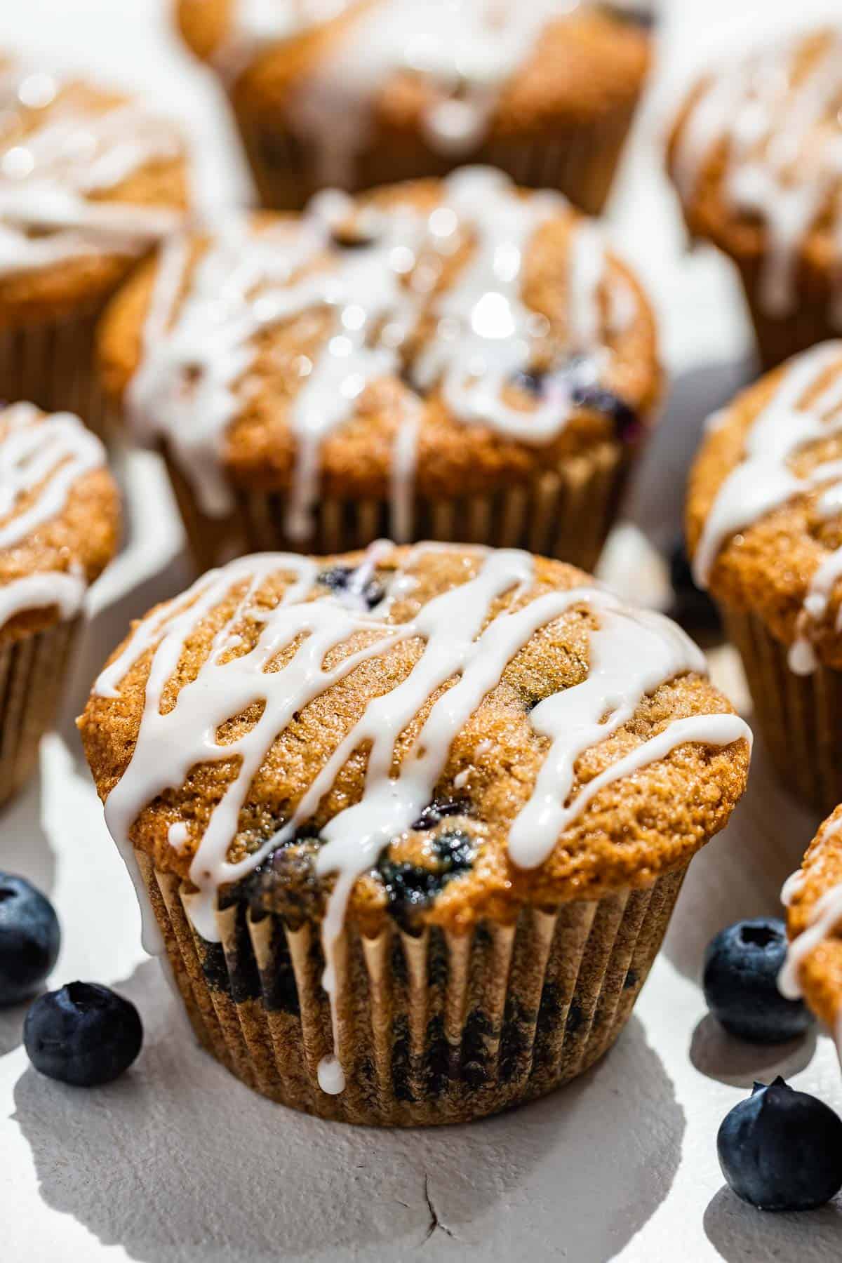 Side view of glazed paleo blueberry muffins on a white background with blueberries around them.