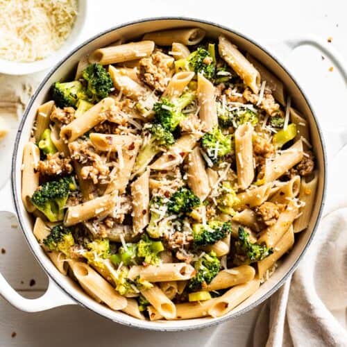 Sausage Broccoli Pasta in a large white pot with grated parmesan cheese on the side.