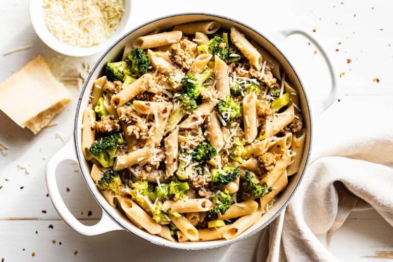 Sausage Broccoli Pasta in a large white pot with grated parmesan cheese on the side.