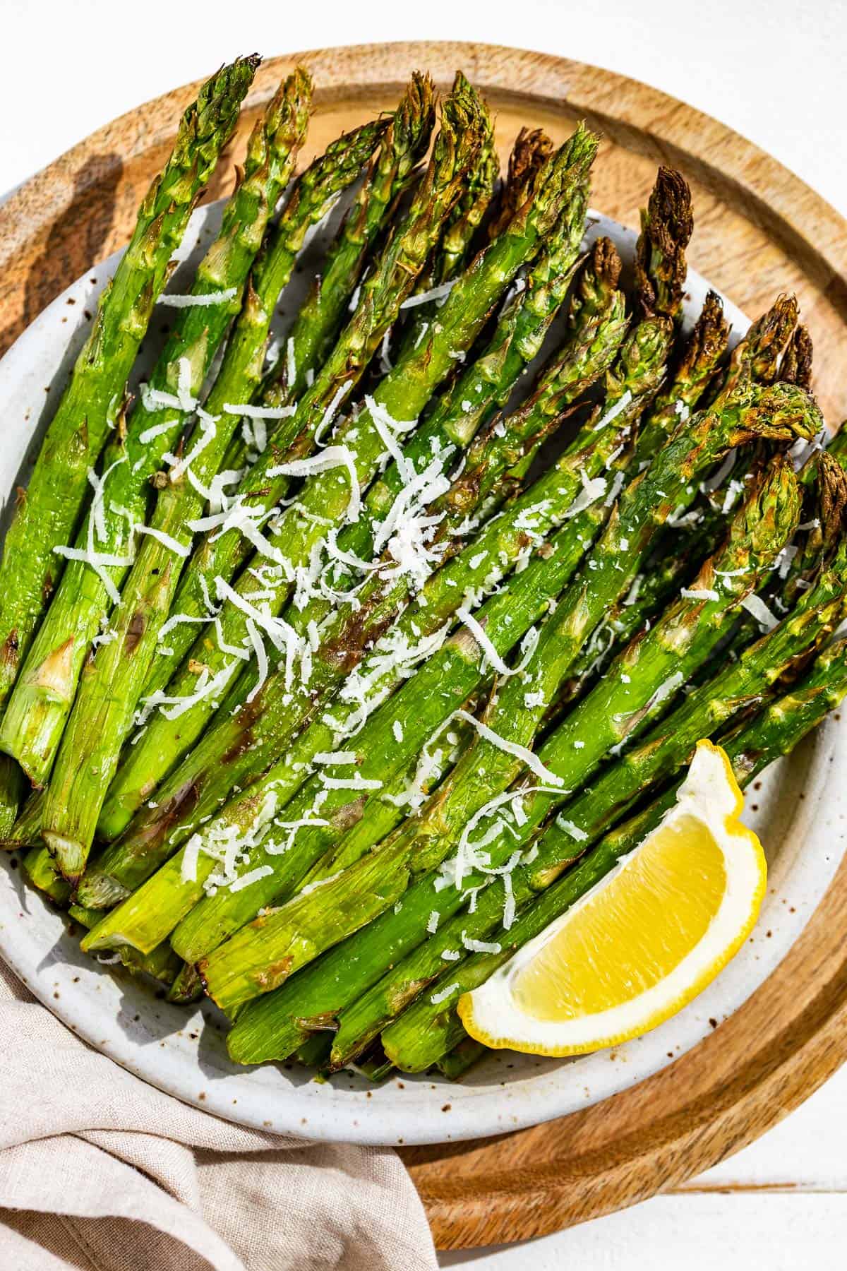 Air fryer asparagus on a pottery plate topped with parmesan and a lemon wedge.